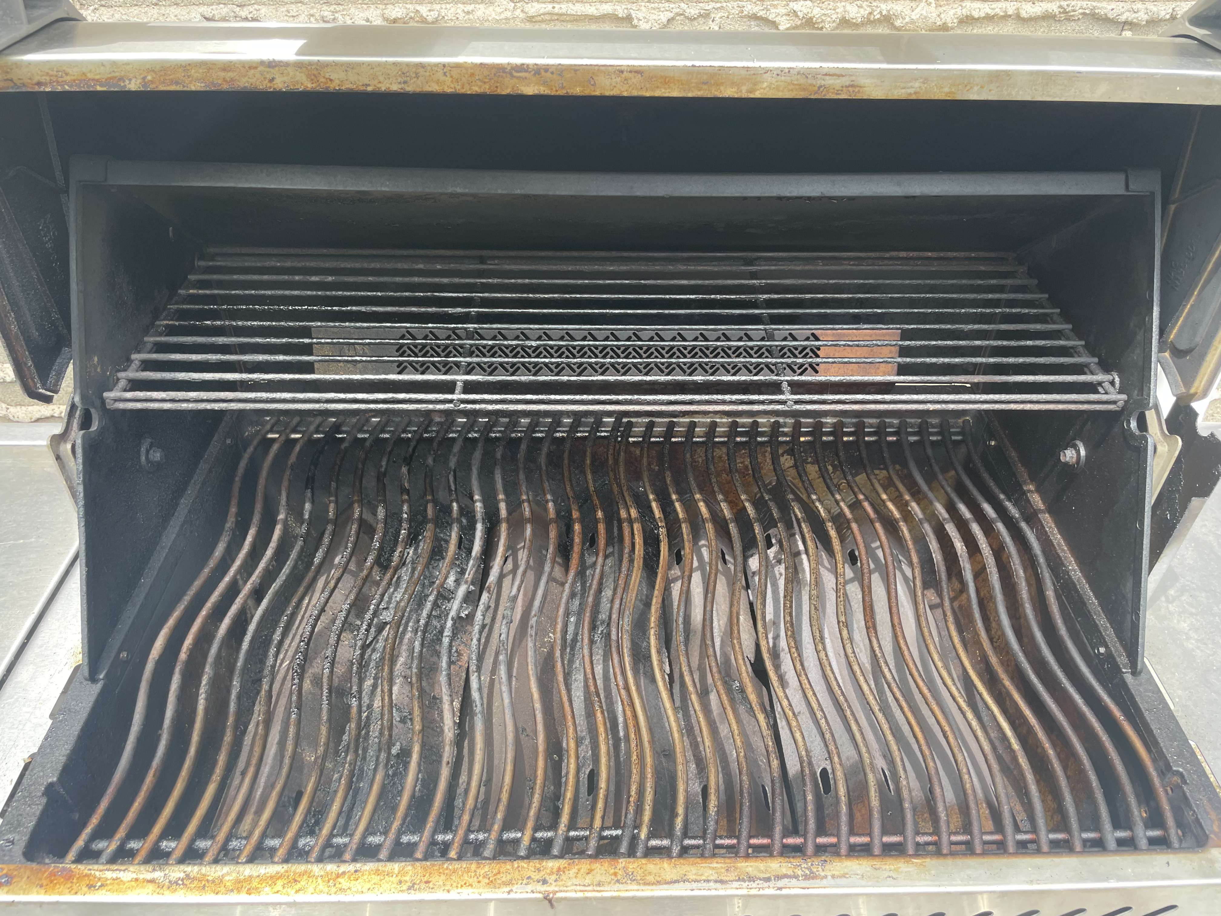 Inside the same Napoleon Prestige before an Aspect deep clean, showing rust-streaked wavy grates, a grease-coated warming rack and a carbon-blackened lid