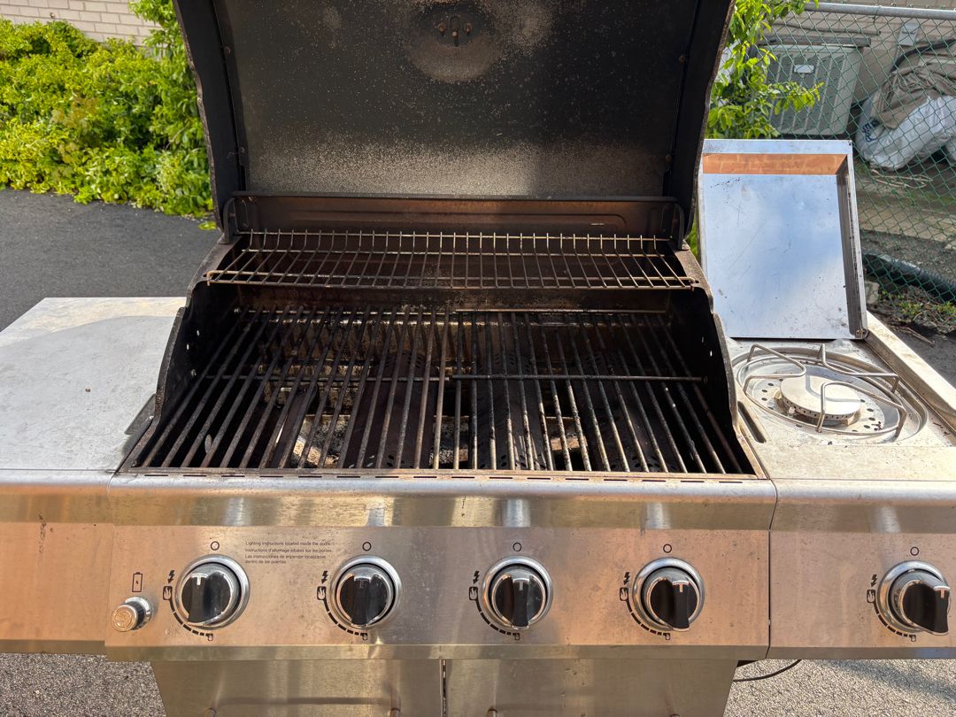 Five-burner Nexgrill before an Aspect deep clean, with a soot-blackened hood, charred cooking grates and burnt-on drippings across the burner box